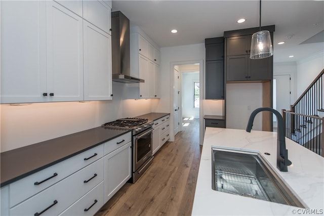 kitchen with high end stove, a sink, decorative light fixtures, wood finished floors, and wall chimney range hood