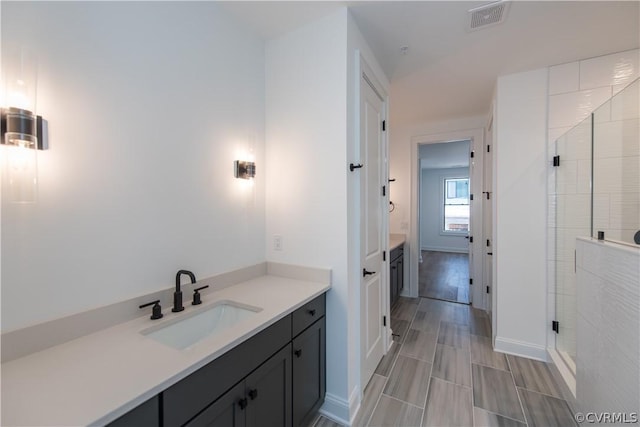 bathroom featuring visible vents, baseboards, wood tiled floor, a stall shower, and vanity