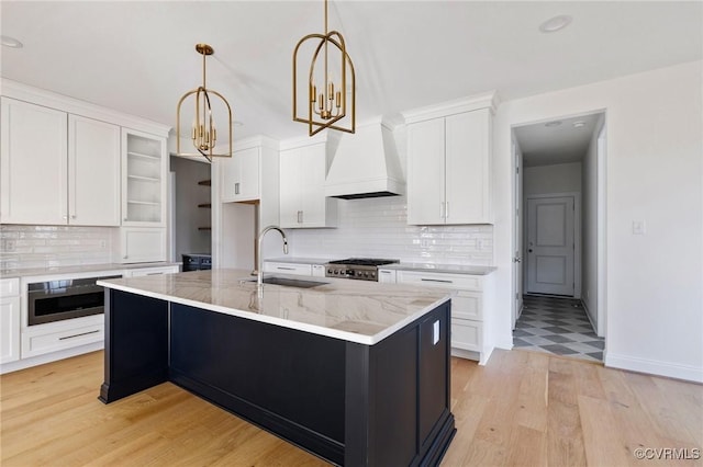 kitchen featuring custom exhaust hood, sink, pendant lighting, a center island with sink, and white cabinets