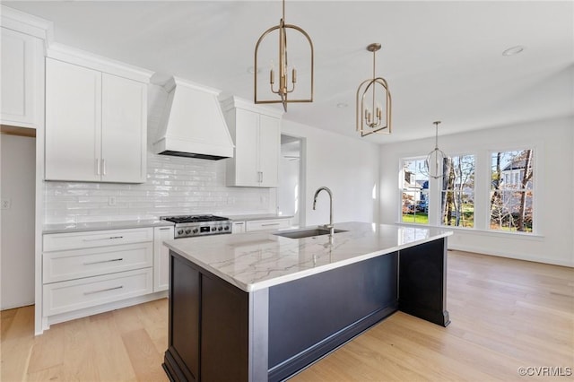 kitchen with sink, hanging light fixtures, custom range hood, light hardwood / wood-style floors, and white cabinetry