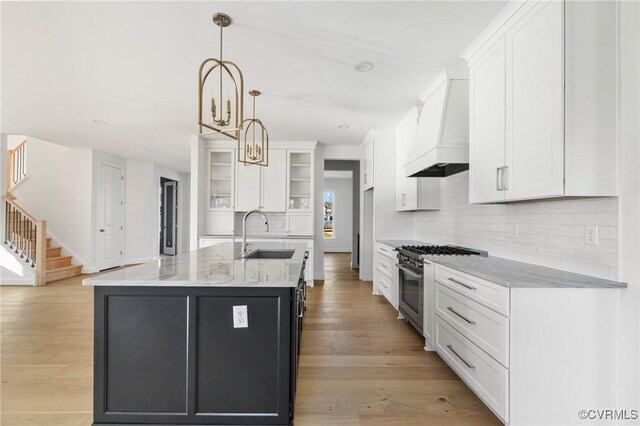 kitchen with stainless steel range, sink, light hardwood / wood-style flooring, a center island with sink, and custom range hood