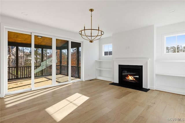 unfurnished living room with light hardwood / wood-style floors, a healthy amount of sunlight, and an inviting chandelier