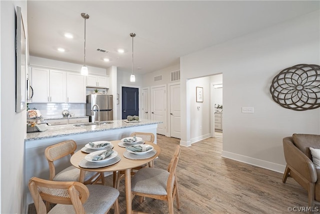 kitchen with sink, hanging light fixtures, light hardwood / wood-style flooring, stainless steel fridge, and white cabinets