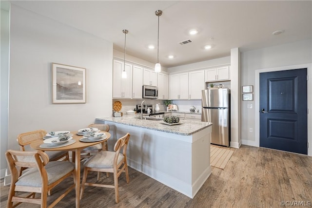 kitchen with kitchen peninsula, light hardwood / wood-style floors, decorative light fixtures, white cabinets, and appliances with stainless steel finishes