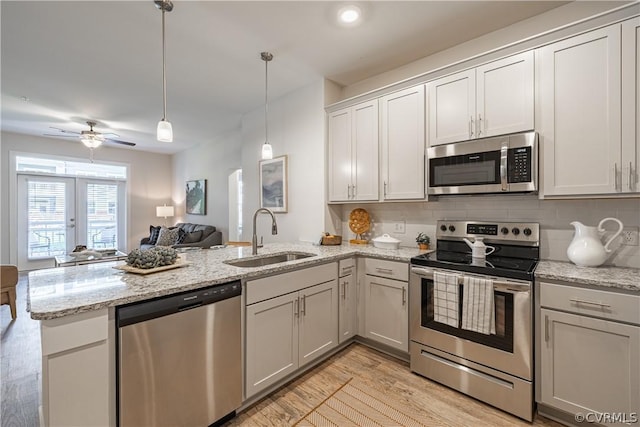 kitchen with sink, hanging light fixtures, stainless steel appliances, kitchen peninsula, and light wood-type flooring