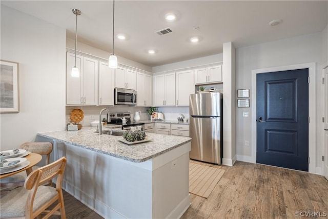 kitchen featuring kitchen peninsula, stainless steel appliances, sink, decorative light fixtures, and white cabinetry