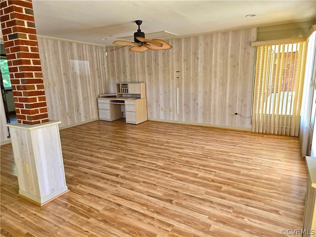 unfurnished living room featuring ceiling fan, wooden walls, a healthy amount of sunlight, and light hardwood / wood-style flooring