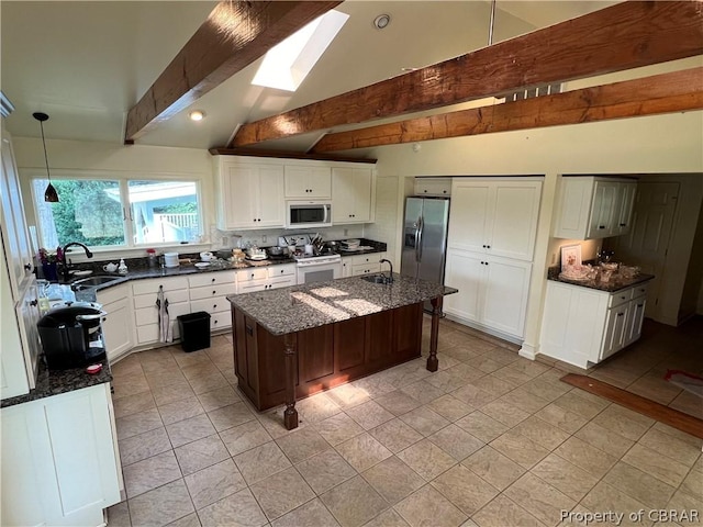 kitchen featuring a kitchen island with sink, sink, stainless steel appliances, and dark stone countertops