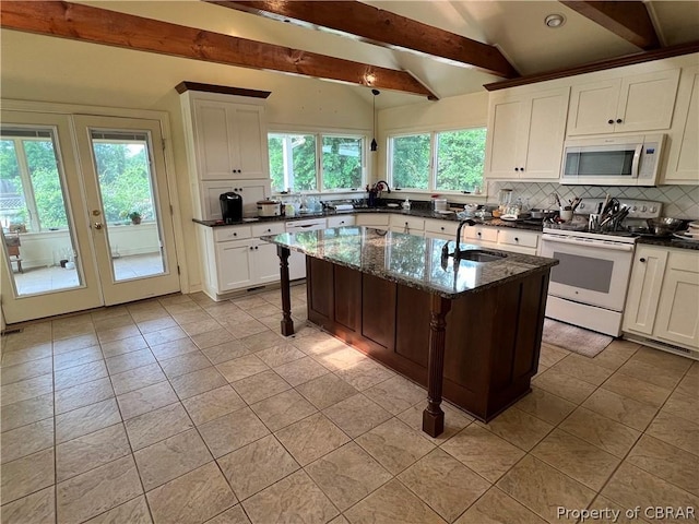 kitchen featuring an island with sink, sink, a breakfast bar area, dark stone countertops, and white appliances