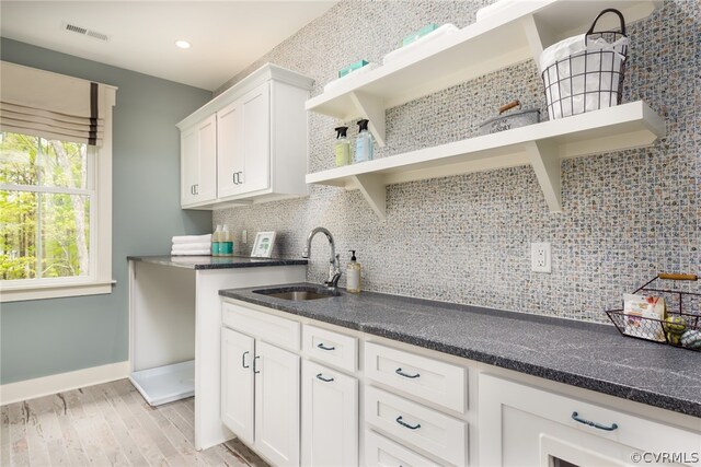 kitchen featuring dark stone counters, light hardwood / wood-style floors, tasteful backsplash, sink, and white cabinetry