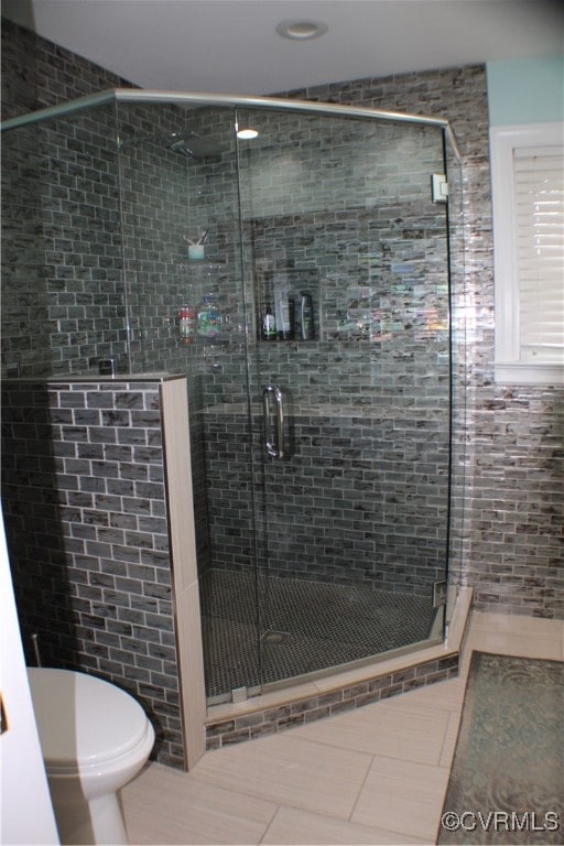 bathroom with tile patterned floors, toilet, and a shower with door