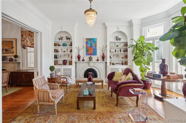 living area with hardwood / wood-style floors, crown molding, built in shelves, and a notable chandelier