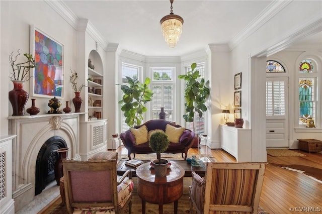 sitting room with light hardwood / wood-style flooring, built in features, a fireplace, ornamental molding, and a chandelier