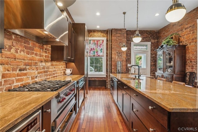 kitchen featuring sink, brick wall, hanging light fixtures, and wall chimney range hood