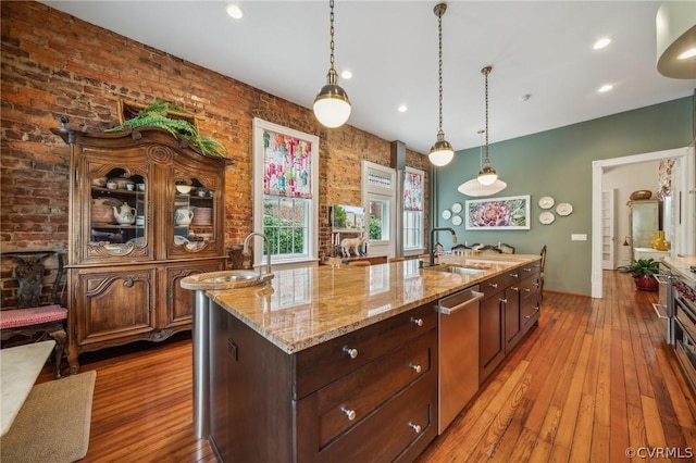 kitchen with stainless steel dishwasher, sink, wood-type flooring, a center island with sink, and hanging light fixtures