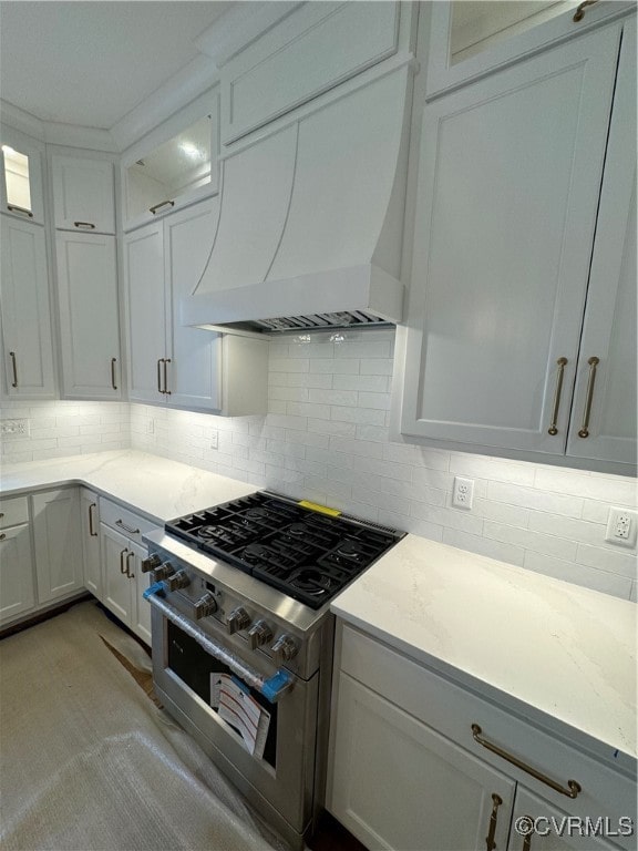 kitchen with high end stove, premium range hood, white cabinets, and backsplash