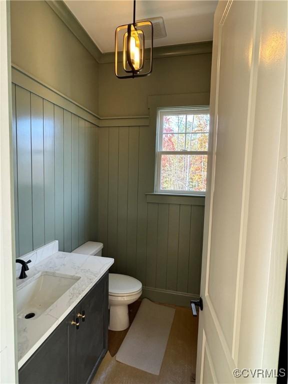 bathroom with vanity, toilet, and wood walls