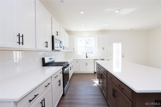 kitchen with dark wood-type flooring, white cabinets, a kitchen island, backsplash, and appliances with stainless steel finishes