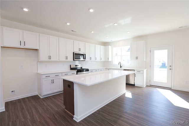 kitchen with a kitchen island, white cabinetry, appliances with stainless steel finishes, backsplash, and dark hardwood / wood-style floors