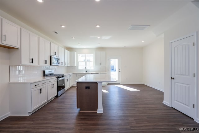 kitchen with white cabinetry, stainless steel appliances, a kitchen island, and dark hardwood / wood-style flooring