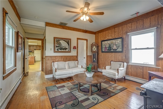 living room with a baseboard radiator, light wood-type flooring, wood walls, and ceiling fan