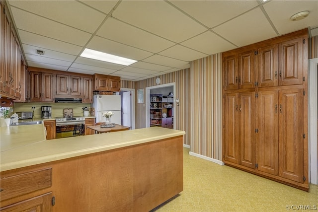 kitchen with white refrigerator, kitchen peninsula, stainless steel range with electric stovetop, a drop ceiling, and ventilation hood