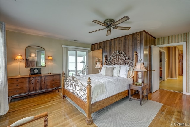 bedroom featuring wooden walls, light wood-type flooring, and ceiling fan