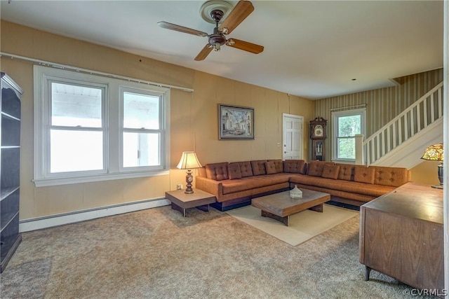 living area with stairway, baseboard heating, carpet flooring, and a ceiling fan