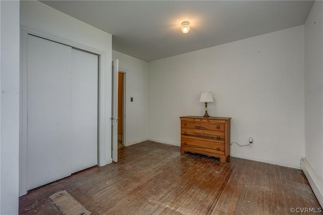 bedroom with baseboard heating, baseboards, a closet, and wood-type flooring