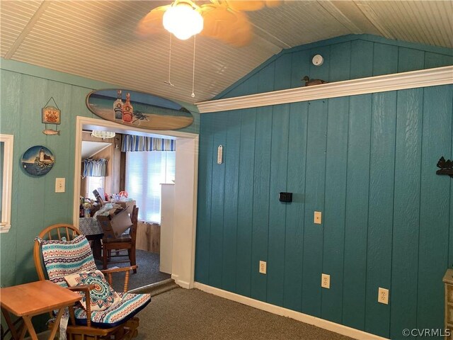 sitting room featuring carpet, wooden walls, ceiling fan, and vaulted ceiling