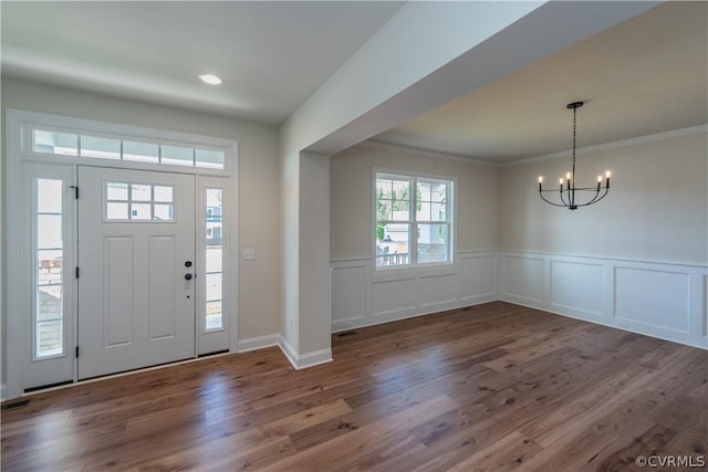 foyer with dark wood-type flooring, a notable chandelier, and crown molding