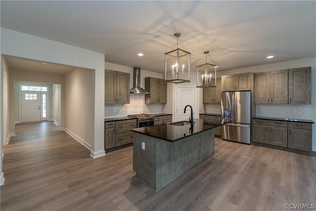 kitchen featuring a kitchen island with sink, stainless steel appliances, sink, wall chimney range hood, and decorative light fixtures