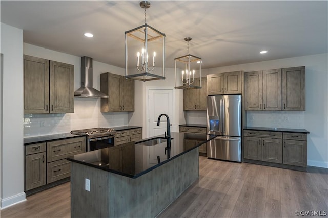 kitchen featuring stainless steel appliances, sink, decorative light fixtures, wall chimney exhaust hood, and a kitchen island with sink