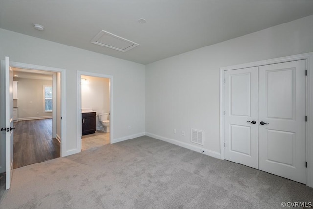 unfurnished bedroom featuring ensuite bathroom, a closet, and light carpet