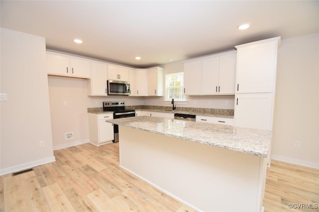 kitchen featuring light stone countertops, white cabinetry, a center island, light hardwood / wood-style floors, and appliances with stainless steel finishes