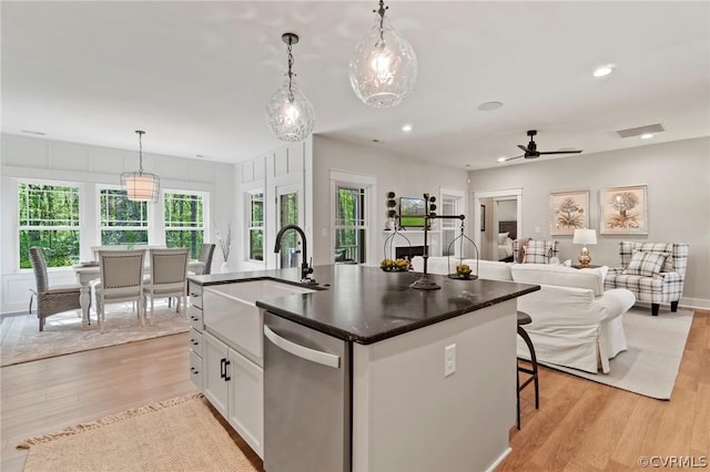 kitchen with stainless steel dishwasher, a kitchen island with sink, ceiling fan, pendant lighting, and white cabinetry