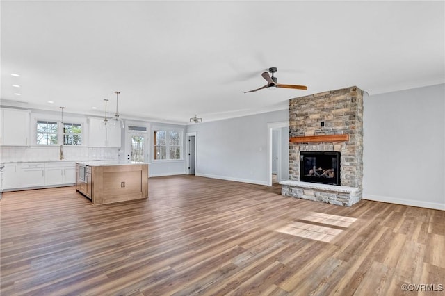 unfurnished living room featuring ceiling fan, a stone fireplace, light wood-type flooring, and ornamental molding