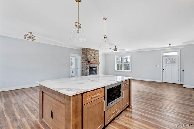 kitchen with pendant lighting, stainless steel microwave, a stone fireplace, light hardwood / wood-style flooring, and ceiling fan