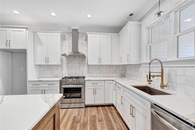 kitchen featuring appliances with stainless steel finishes, wall chimney exhaust hood, sink, decorative light fixtures, and white cabinetry