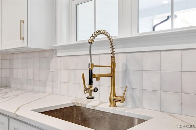 room details featuring white cabinets, backsplash, light stone countertops, and sink