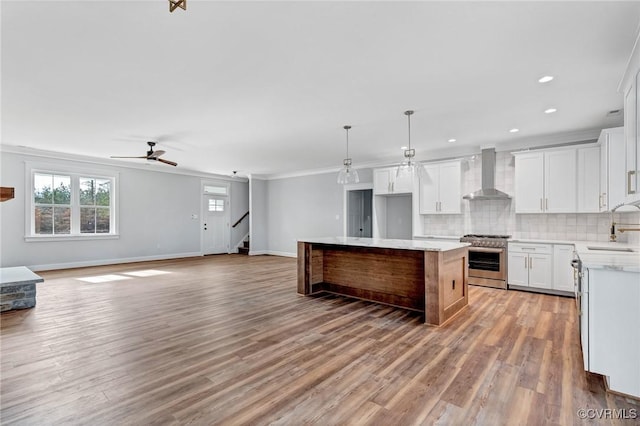 kitchen with wall chimney exhaust hood, high end stove, wood-type flooring, a center island, and white cabinetry