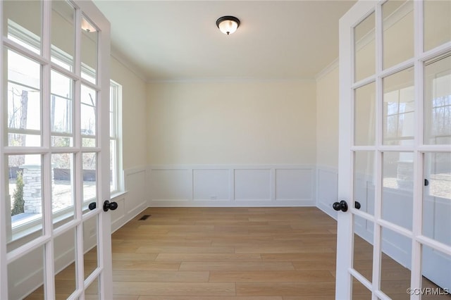 empty room featuring crown molding, french doors, and light wood-type flooring