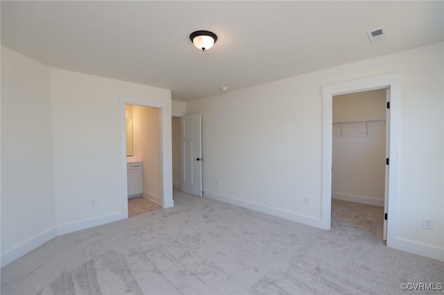 unfurnished bedroom with ensuite bathroom, a walk in closet, light carpet, and a closet