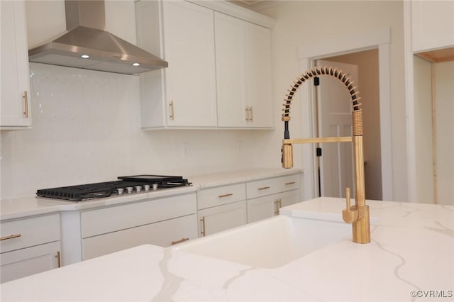 kitchen with white cabinetry, wall chimney range hood, light stone countertops, and stainless steel gas stovetop