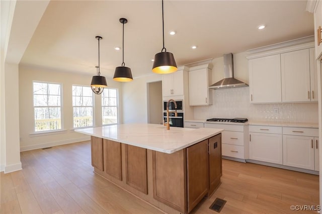 kitchen featuring pendant lighting, white cabinetry, a large island, light stone counters, and wall chimney exhaust hood