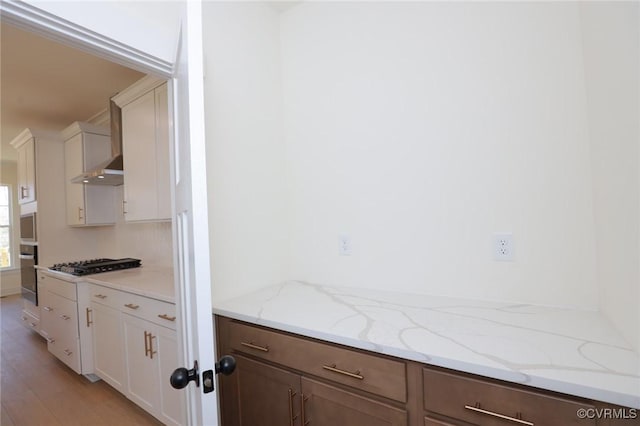 kitchen with white cabinets, wall oven, light stone counters, gas stovetop, and light hardwood / wood-style flooring