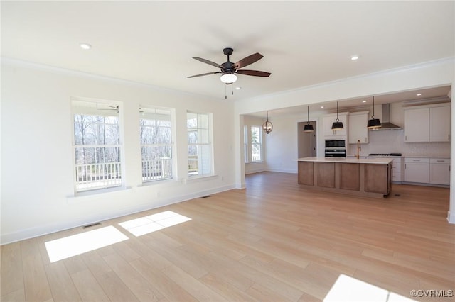 unfurnished living room with crown molding, ceiling fan, sink, and light wood-type flooring