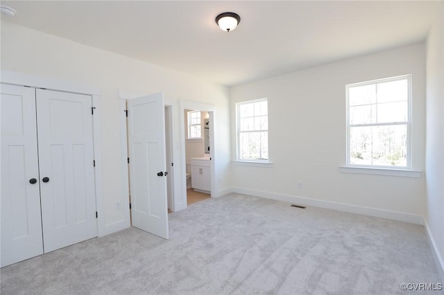 unfurnished bedroom with light carpet, ensuite bath, and a closet