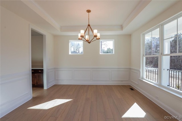 spare room featuring a tray ceiling, light hardwood / wood-style floors, and an inviting chandelier