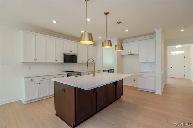 kitchen with hanging light fixtures, white cabinets, light hardwood / wood-style floors, electric range, and a kitchen island with sink